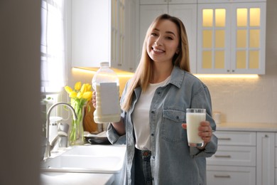 Photo of Young woman with gallon bottle of milk and glass near white countertop in kitchen