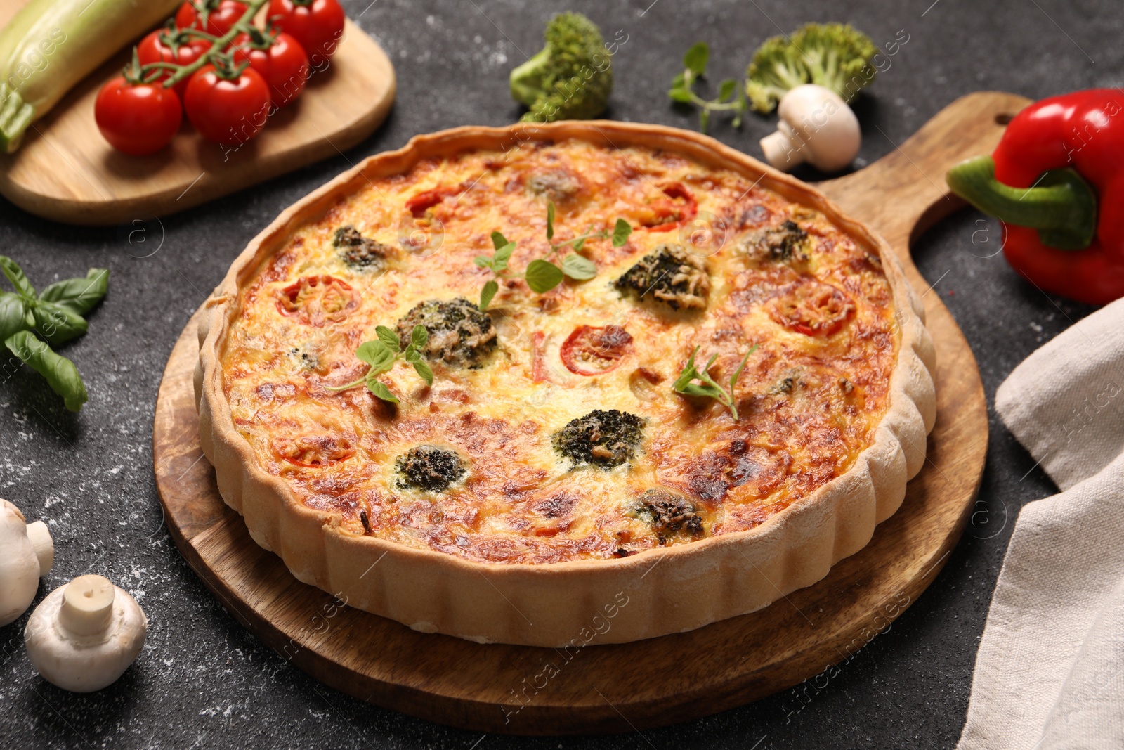 Photo of Delicious homemade vegetable quiche, oregano and mushrooms on black table