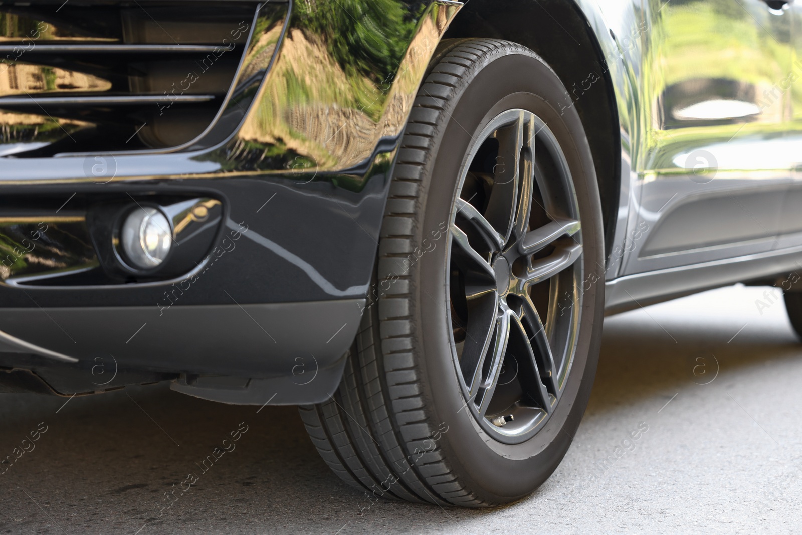 Photo of Modern black car parked on asphalt road outdoors, closeup