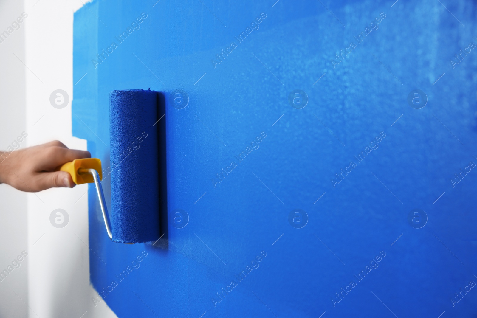 Photo of Man painting white wall with blue dye, closeup. Interior renovation