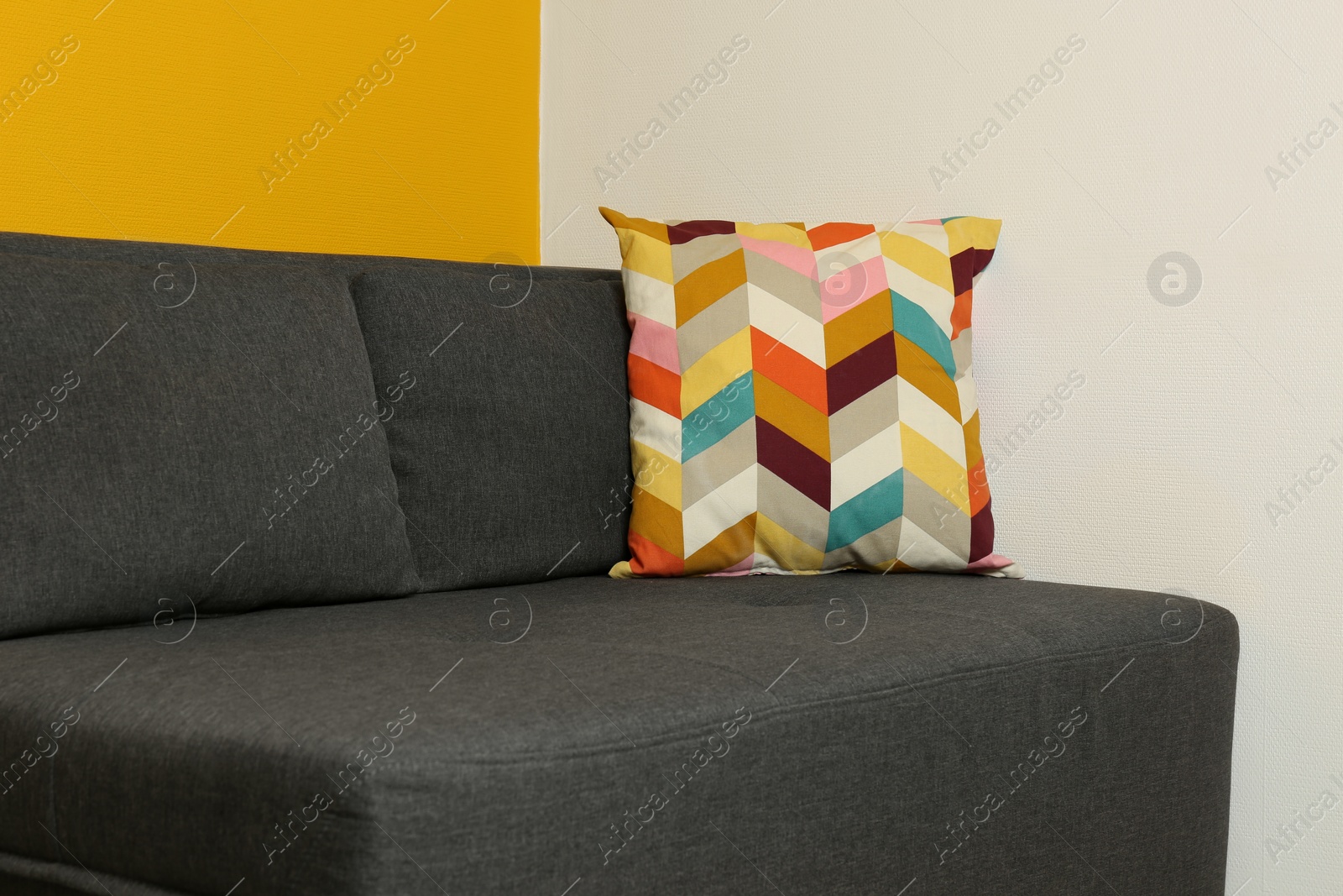 Photo of Stylish grey sofa with bright cushion in room