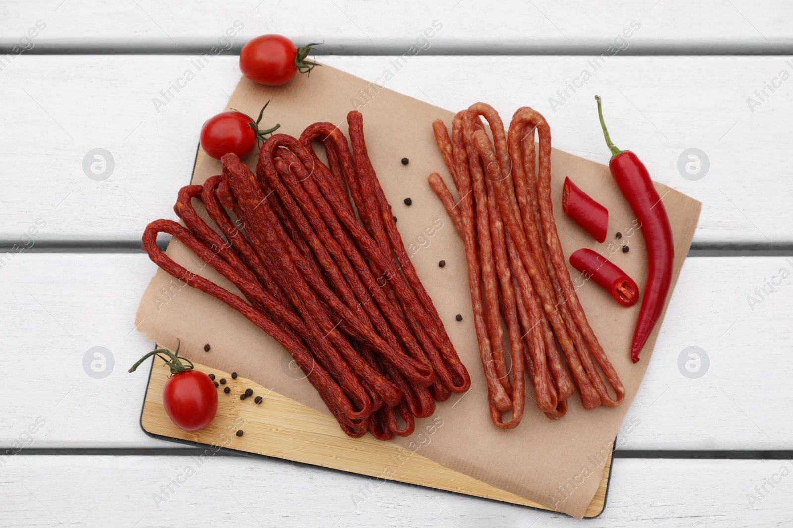 Photo of Delicious kabanosy with tomatoes, peppercorn and chilli on white wooden table, top view