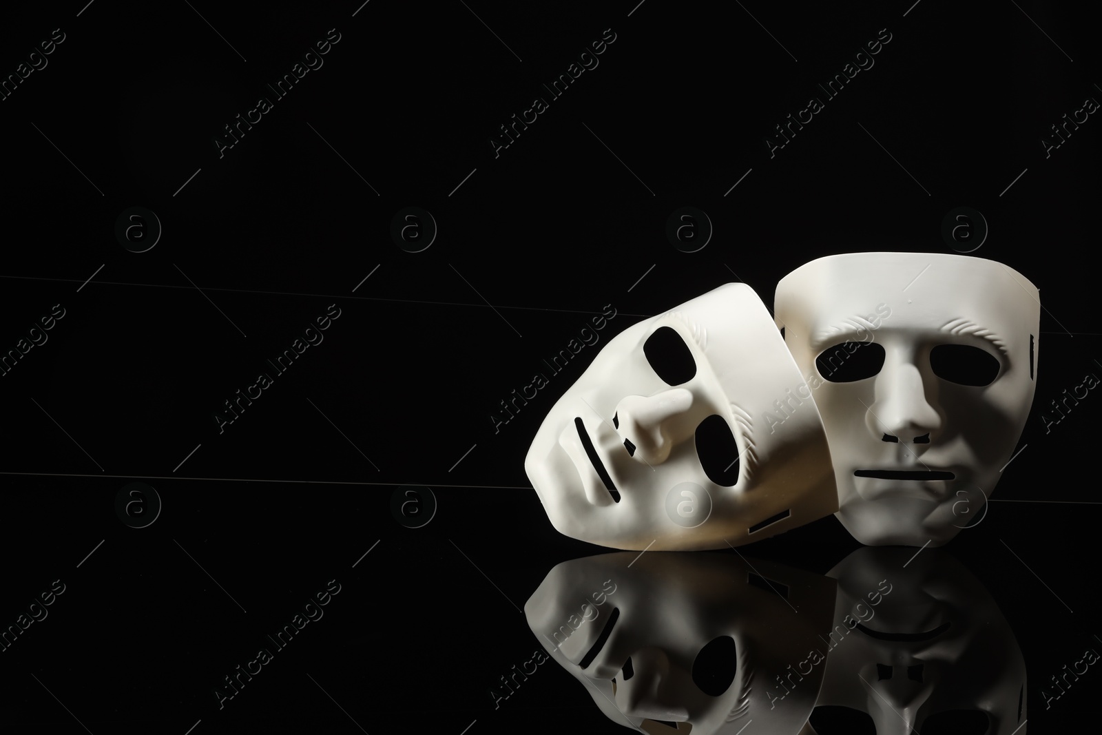 Photo of Plastic face masks on black mirror surface, space for text. Theatrical performance