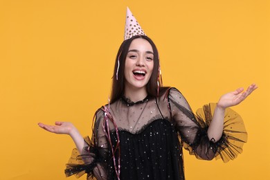 Happy woman in party hat with streamers on orange background