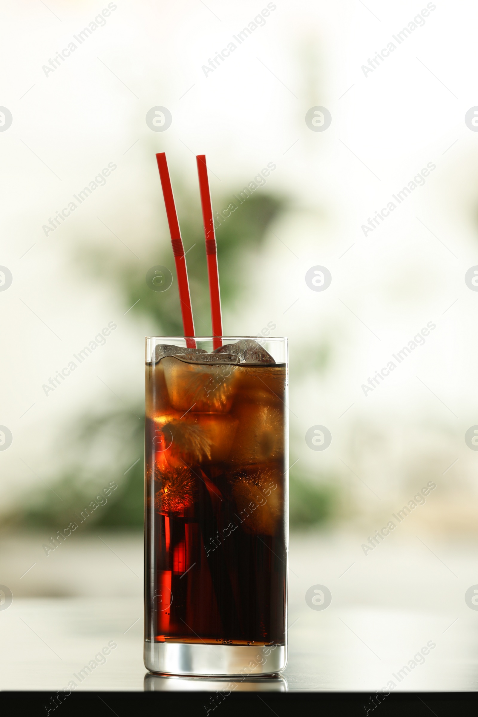 Photo of Glass of cola with ice on table against blurred background