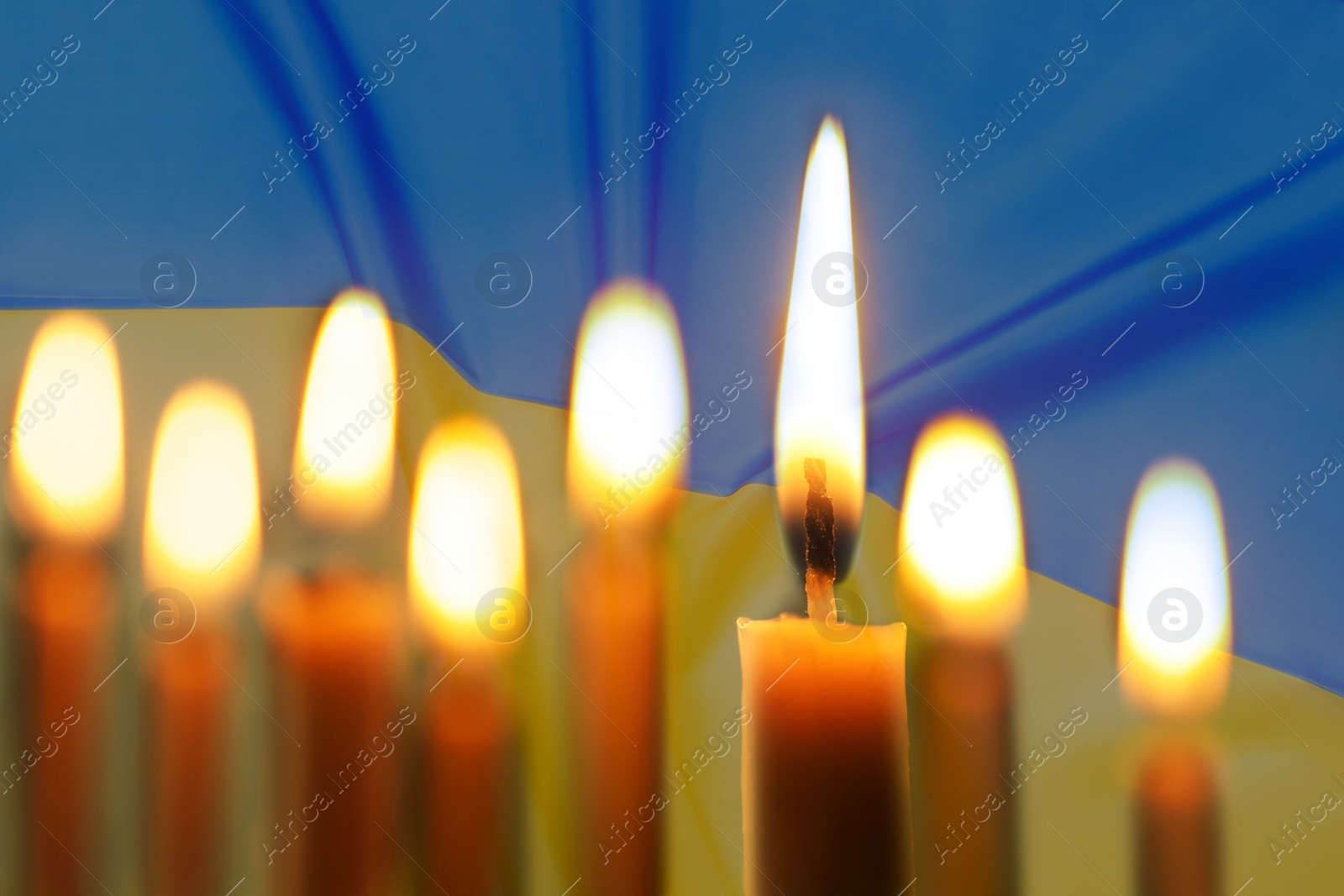 Image of Burning candles and Ukrainian national flag on background, closeup