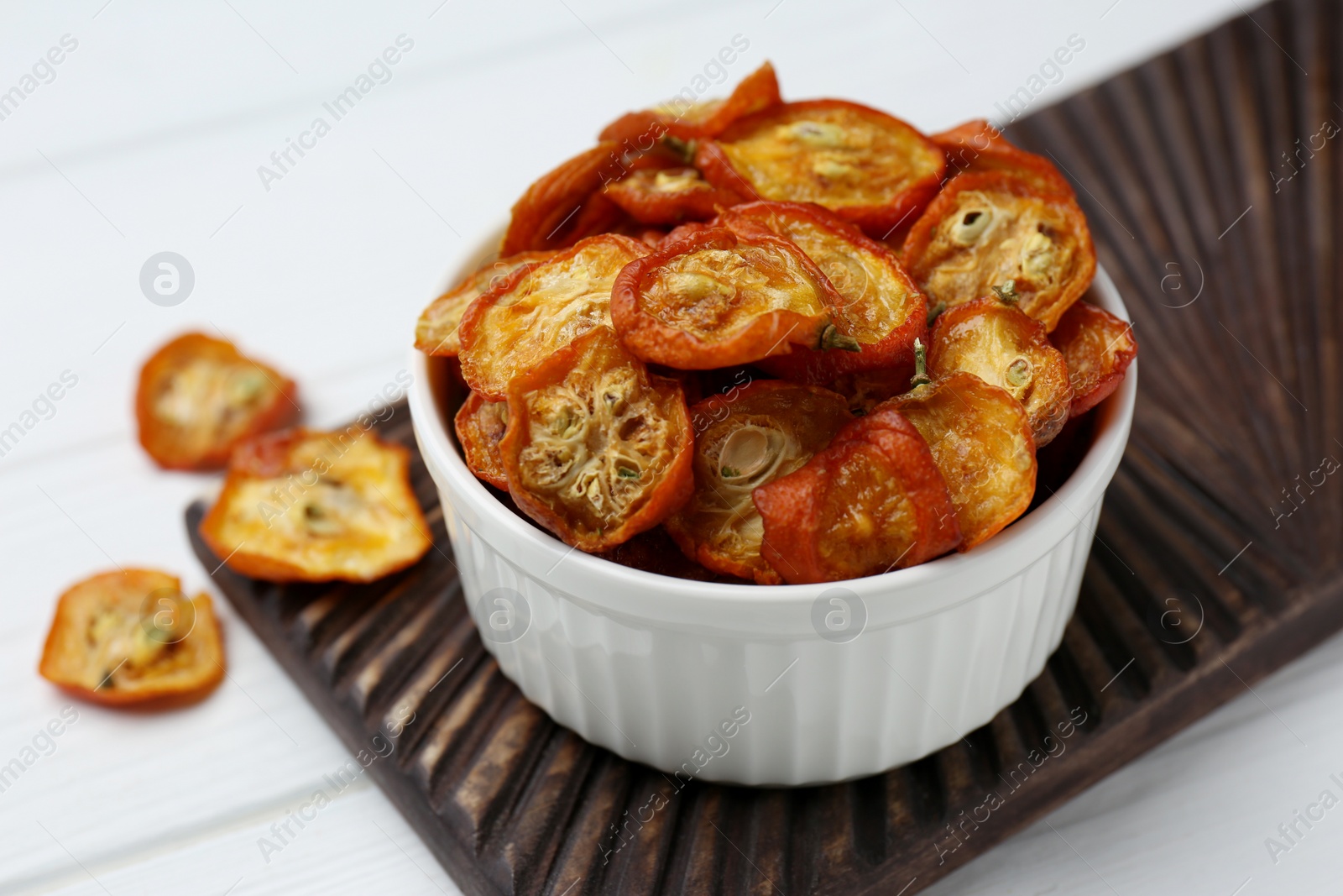 Photo of Bowl with cut dried kumquat fruits on white wooden table, closeup