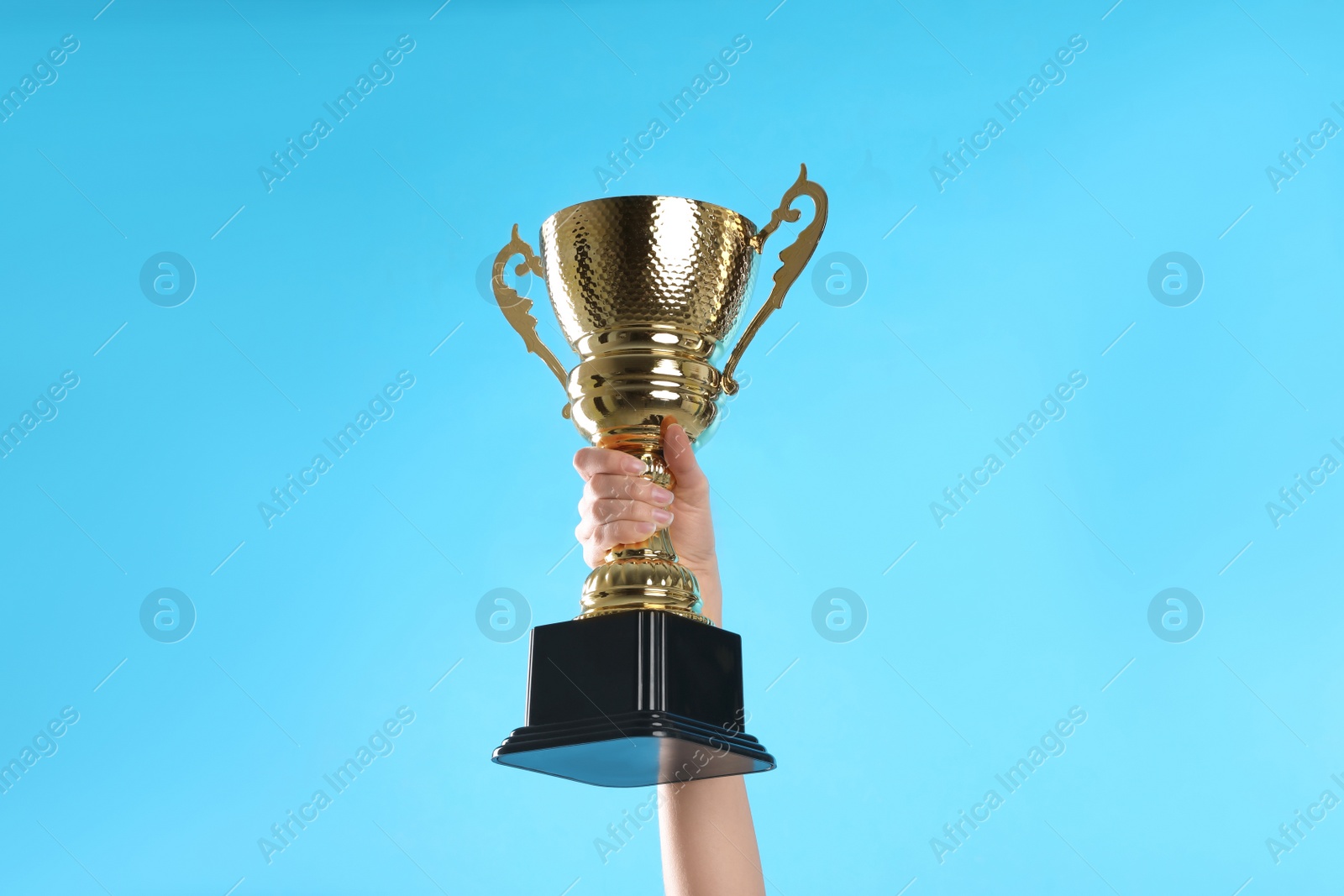 Photo of Woman holding gold trophy cup on light blue background, closeup