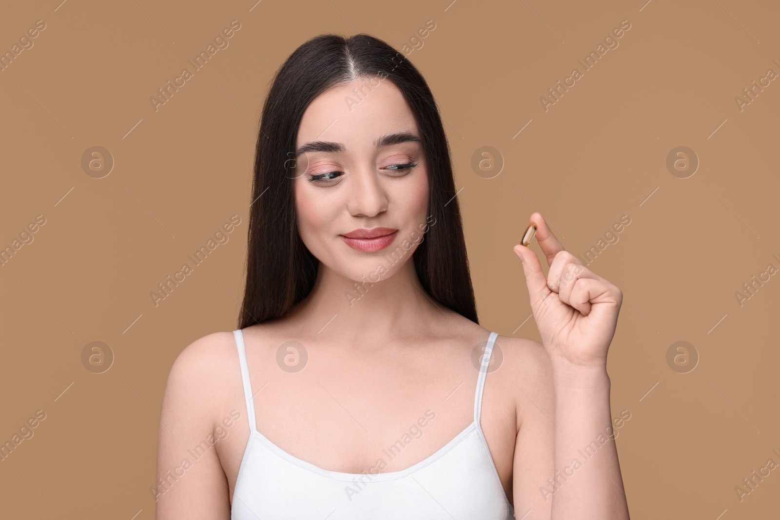 Photo of Beautiful young woman with vitamin pill on beige background