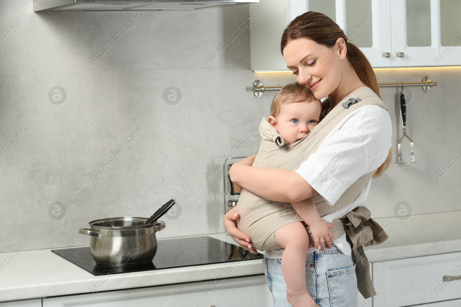 Photo of Mother holding her child in sling (baby carrier) in kitchen