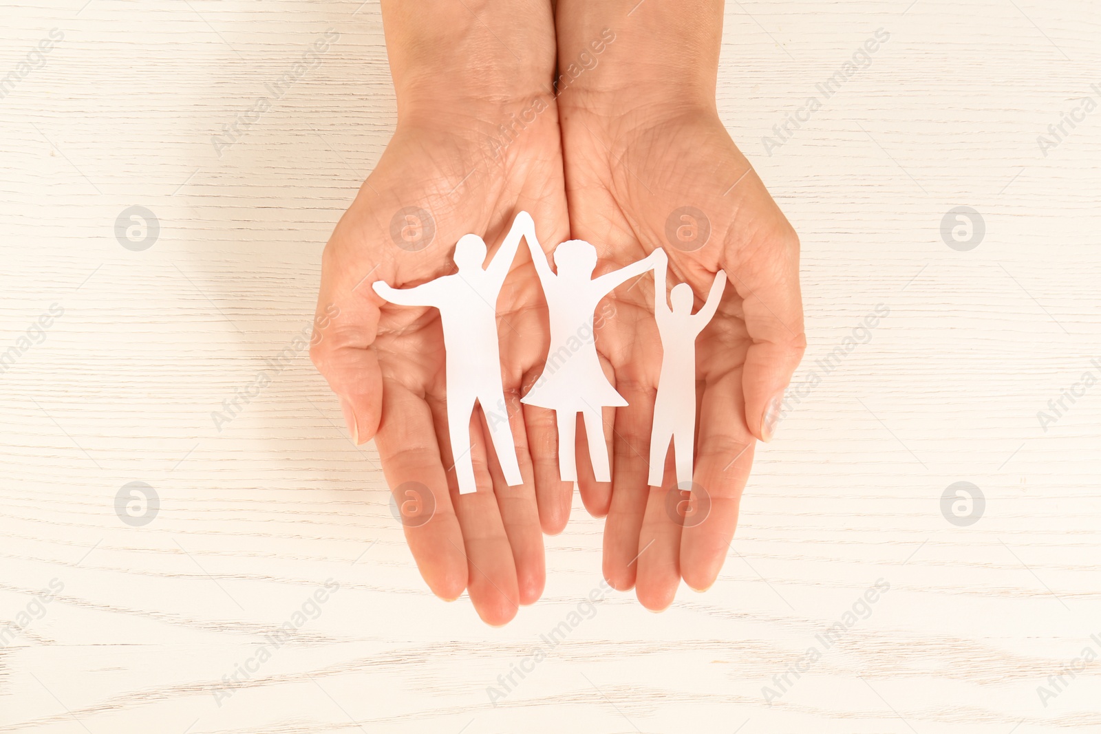 Photo of Woman holding paper figures of happy family in hands on white wooden background, top view