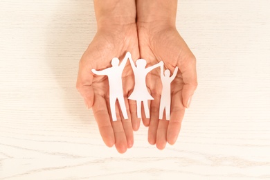 Woman holding paper figures of happy family in hands on white wooden background, top view