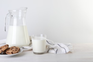Photo of Jug of fresh milk, glass and cookies on wooden table. Space for text