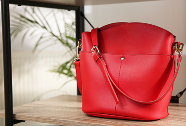 Photo of Stylish red woman's bag on wooden shelf