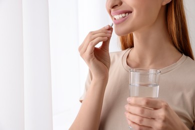 Young woman taking vitamin pill at home, closeup. Space for text