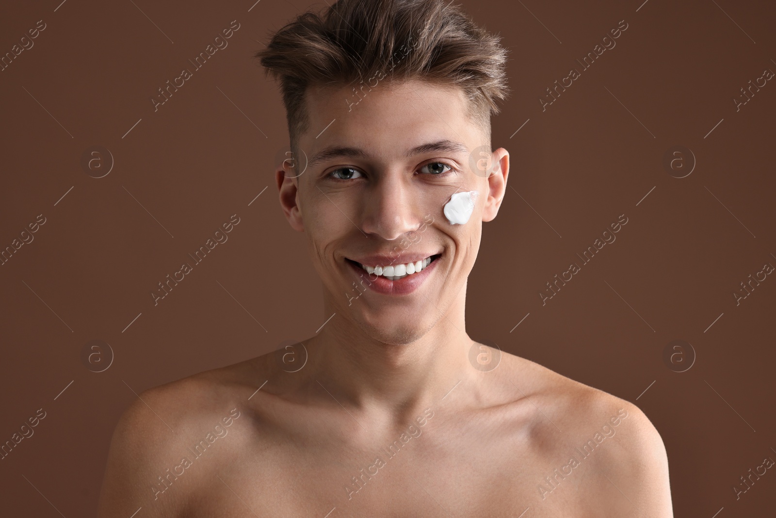 Photo of Handsome man with moisturizing cream on his face against brown background