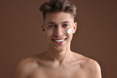 Handsome man with moisturizing cream on his face against brown background
