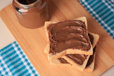 Photo of Tasty toasts with chocolate paste and jar of cream on beige table, above view