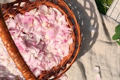 Photo of Wicker basket of beautiful tea rose petals on beige fabric, flat lay