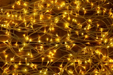 Photo of Glowing Christmas lights on wooden background, top view