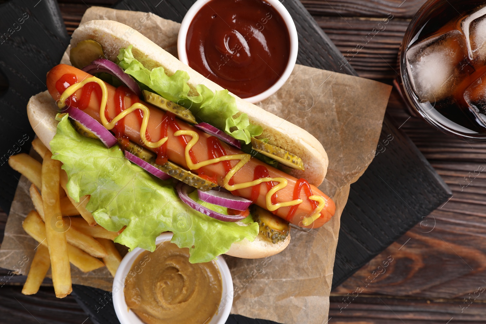 Photo of Delicious hot dog with lettuce, onion and pickle served on wooden table, top view