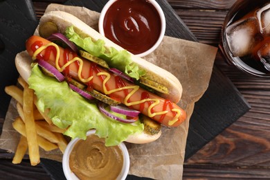 Photo of Delicious hot dog with lettuce, onion and pickle served on wooden table, top view