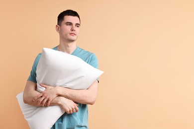 Man in pyjama holding pillow on beige background, space for text