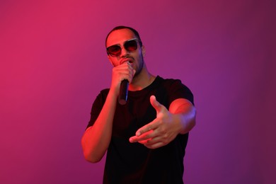 Photo of Handsome man in sunglasses with microphone singing on pink background. Color tone effect