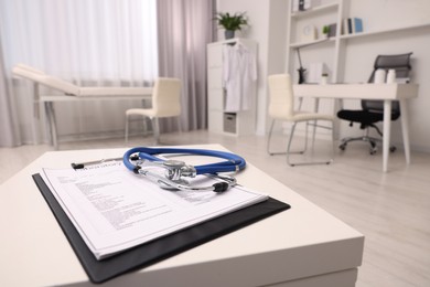 Photo of Clipboard and stethoscope on white table in clinic, space for text. Doctor's workplace