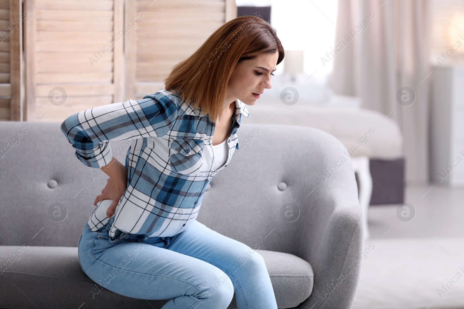 Photo of Young woman suffering from back pain at home