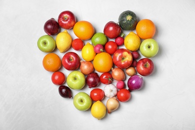 Photo of Heart shaped pile of fruits and vegetables on light background, flat lay