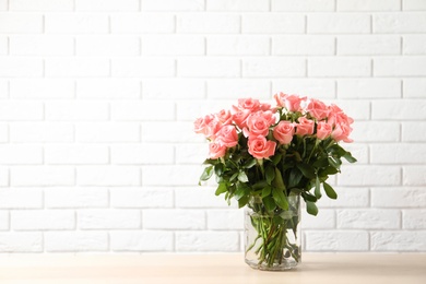 Vase with beautiful rose flowers on table against brick wall background