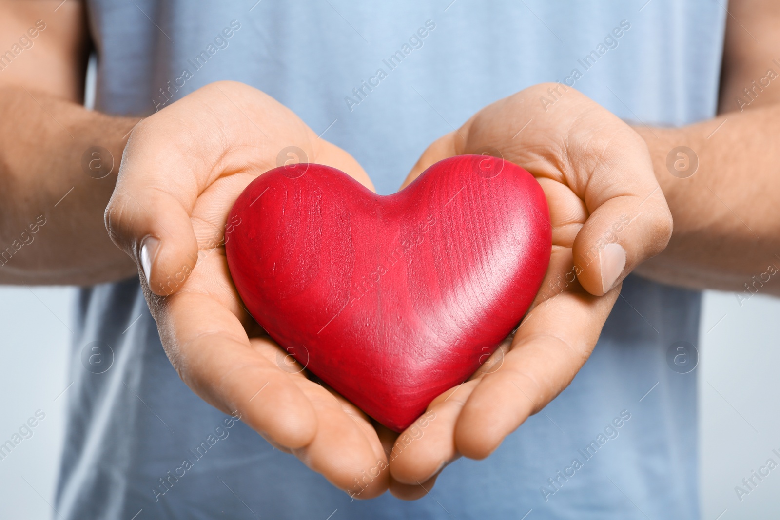 Photo of Young man holding red heart on color background, closeup. Donation concept