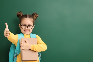 Happy little school child with notebooks showing thumbs up near chalkboard. Space for text