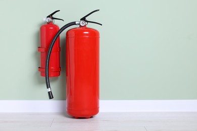 Photo of Red fire extinguishers against light green wall. Space for text