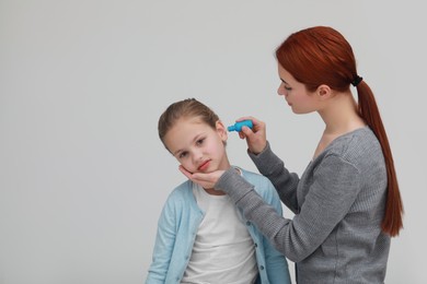 Photo of Mother dripping medication into daughter's ear on light grey background