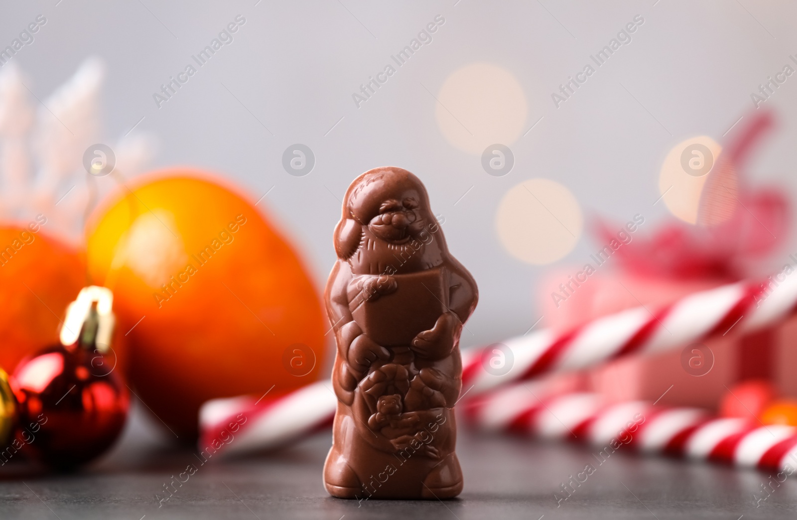 Photo of Chocolate Santa Claus near candy canes and tangerine on grey table