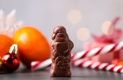 Photo of Chocolate Santa Claus near candy canes and tangerine on grey table