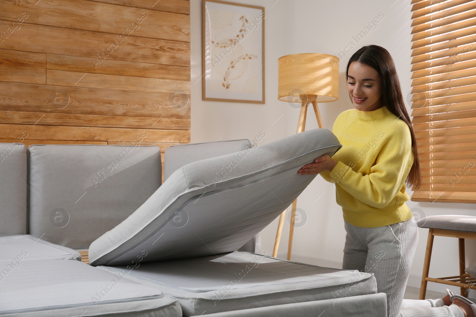 Photo of Young woman unfolding sofa into a bed in room. Modern interior