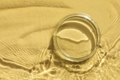 Photo of Stylish presentation for product. Glass podium in water on sand, top view. Space for text