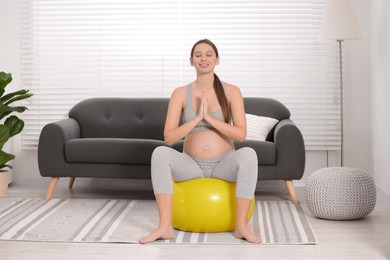 Photo of Pregnant woman meditating on fitness ball in room. Home yoga