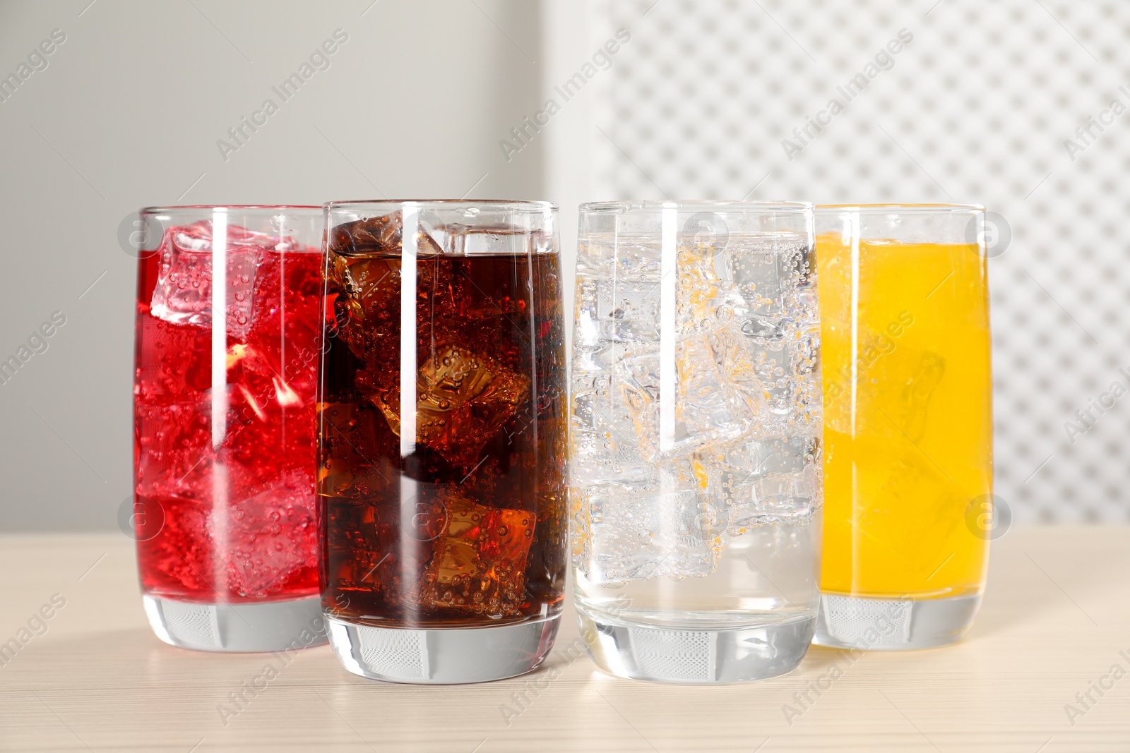 Photo of Glasses of different refreshing soda water with ice cubes on white table