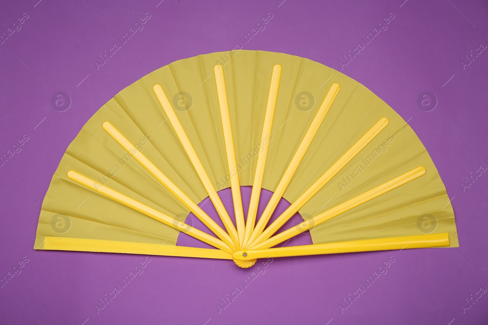 Photo of Bright yellow hand fan on purple background, top view