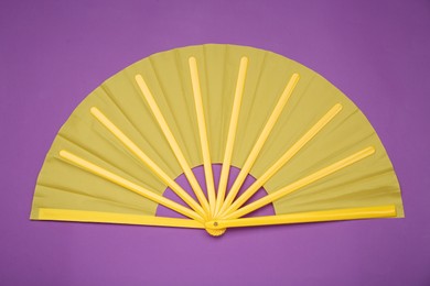 Photo of Bright yellow hand fan on purple background, top view