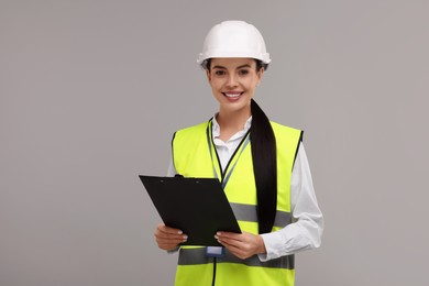 Photo of Engineer in hard hat holding clipboard on grey background
