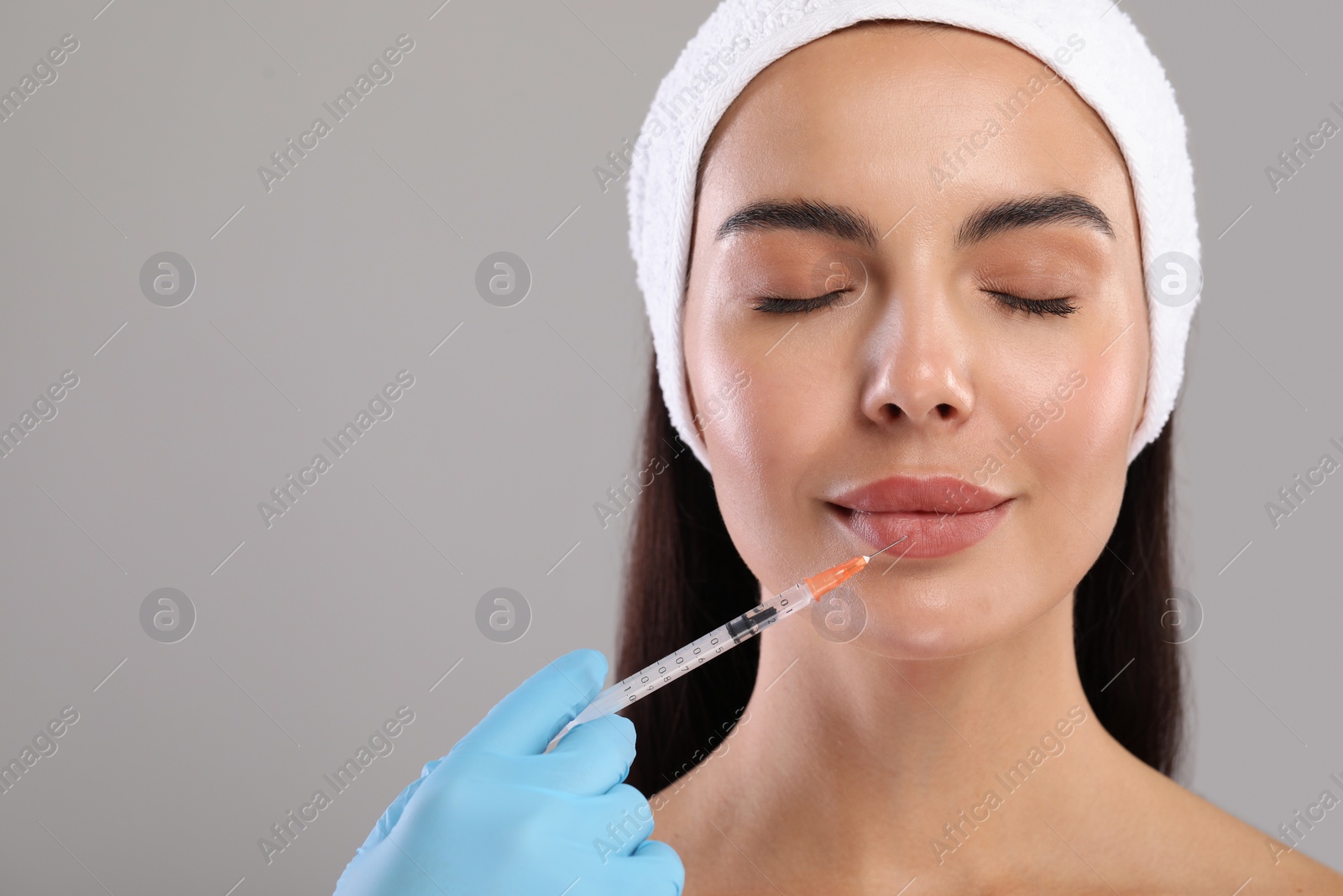 Photo of Doctor giving lips injection to young woman on light grey background, space for text. Cosmetic surgery