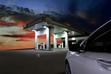Image of Car driving up to modern gas filling station beside the road in evening