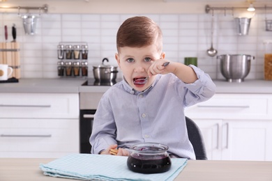 Photo of Cute little boy eating sweet jam at table