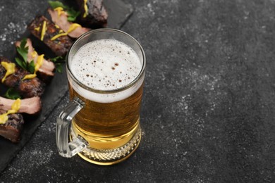 Mug with beer and delicious grilled ribs on dark grey textured table. Space for text