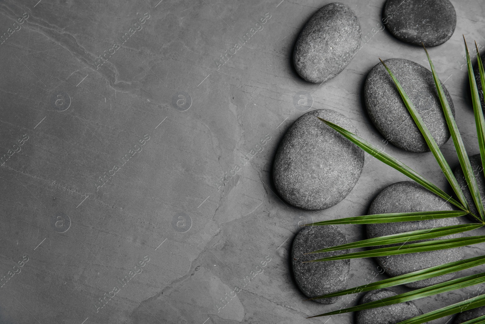 Photo of Zen stones and tropical leaf on dark background, top view with space for text